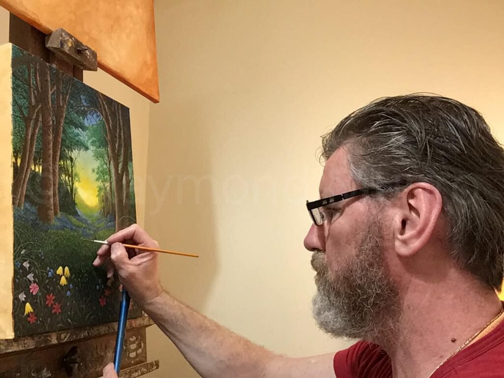 Raymond Munro painting the Woodland Scene, depicting a tranquil woodland with tall trees and dappled sunlight, evoking the peaceful ambiance of the forest.