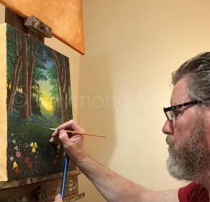 Raymond Munro creating original oil painting of woordland scene with poppies in the foreground. There is a clearing in the background formed by a natural path with trees on each side. The yellow color from the sun is visible in the background.